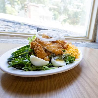 A plate holds cobb salad topped with fried chicken.