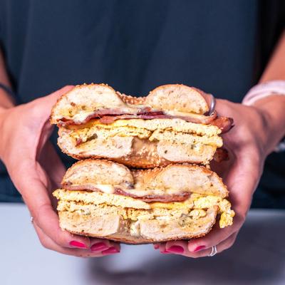Hands holding bagel sandwiches.