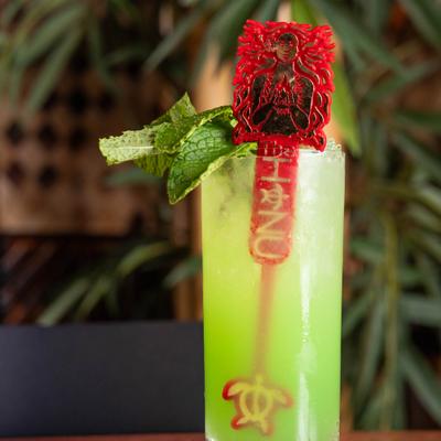Stolen idol cocktail garnished with mint and decorative stirrer.