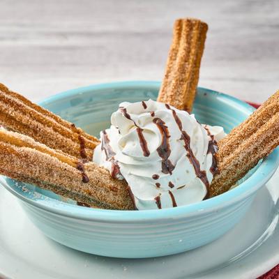 Churros topped with whipped cream and chocolate syrup.
