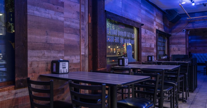 Interior of a restaurant with wooden walls, blue lighting, tables, black chairs