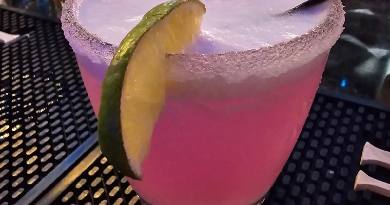 A refreshing pink drink garnished with a lime wedge resting on bar mat