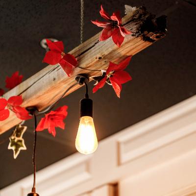 Hanging light bulb with wooden beam and red leaf decor.