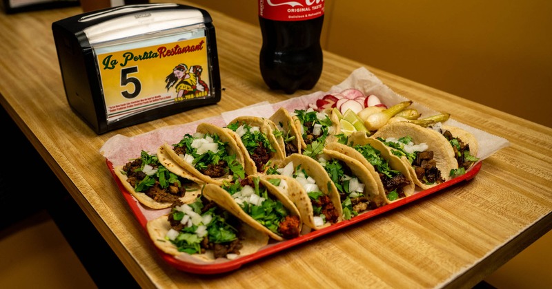 A tray of tacos beside a bottle of soda and napkins