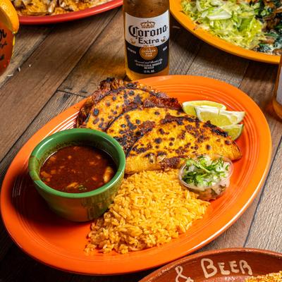 Quesabirria plate on a wooden table with other food plates and a bottle of Mexican beer.