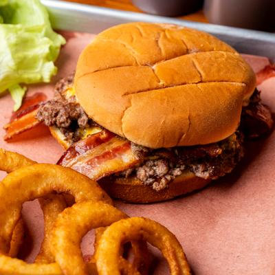 A bacon cheeseburger on pink butcher paper served with golden onion rings.