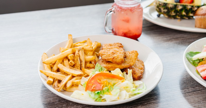 Fish and Chips served with salad, beside a drink and other dishes