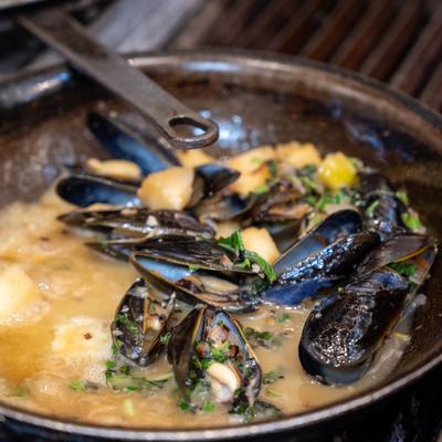 Mussels cooking in a creamy broth in a pan.