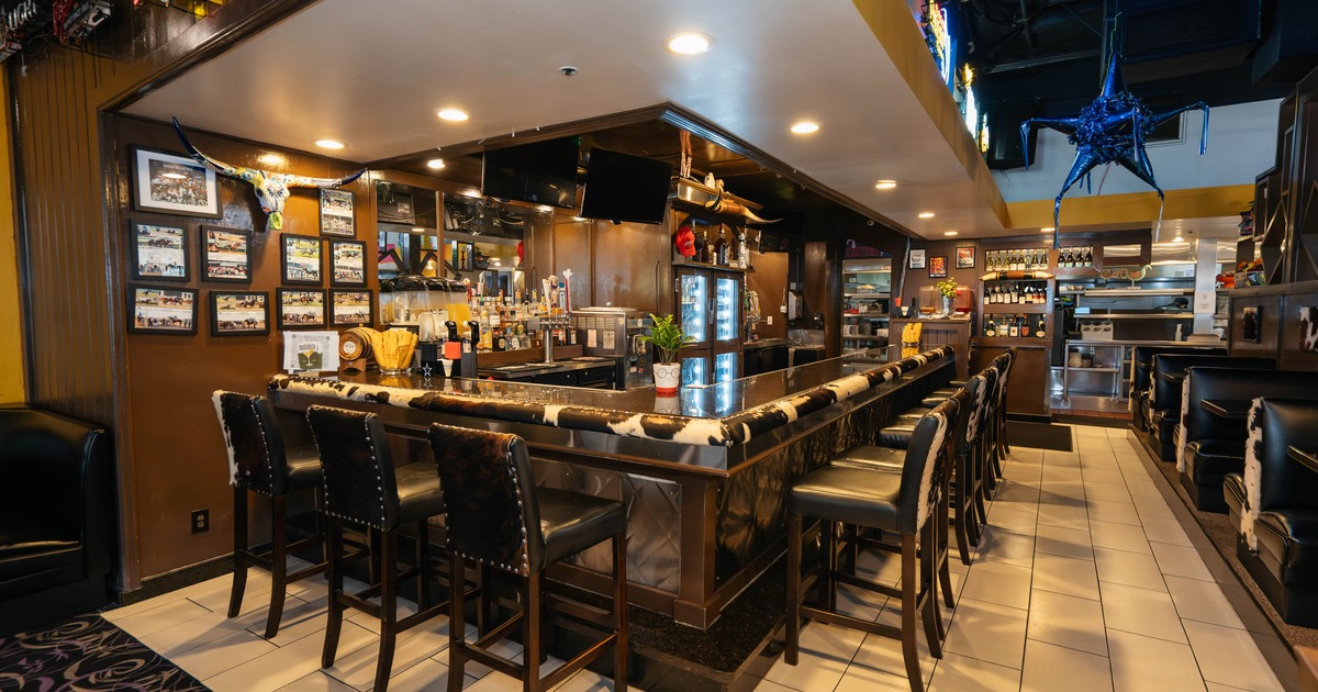 Interior of a bar with a U shaped counter, black leather stools, brown walls with photographs