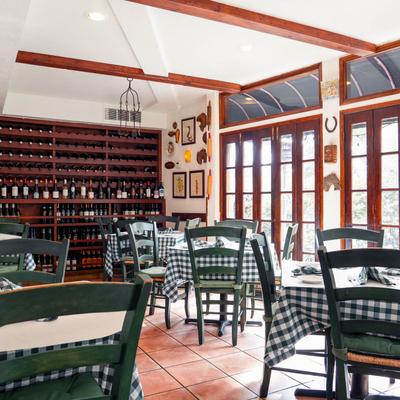 Bright interior with set tables, wooden wine rack, wall art, and large windows.