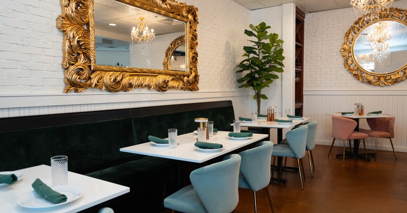 Interior, banquette bench with tables and chairs, large brass framed mirrors, white brick walls