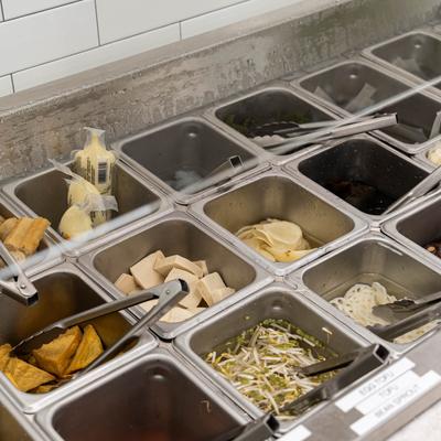 Self-serve ingredient bar with various fresh ingredients in metal bins.