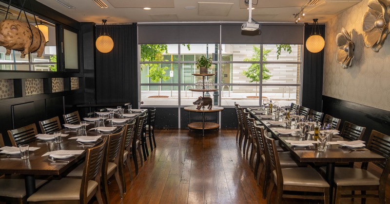 Restaurant dining room with long tables set for dining, chairs, and large windows