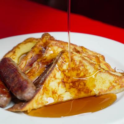 Syrup being poured over French toast with sausage links.