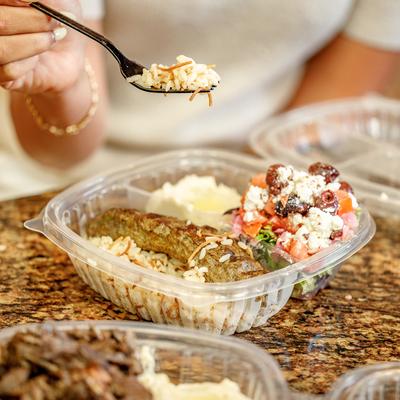 Person holding a fork with rice over a takeaway lamb kebab platter.