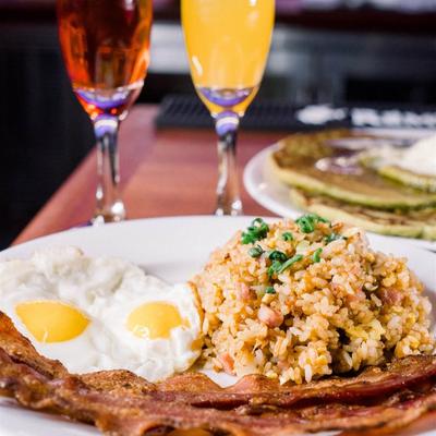 A plate with eggs, rice and bacon, accompanied with two flute drinks and pancakes.