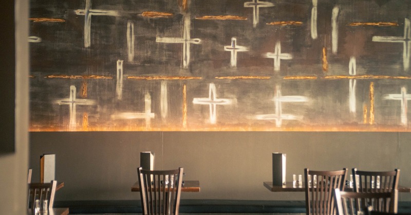 An abstract dark wall art featuring white and orange lines, wooden tables, and chairs
