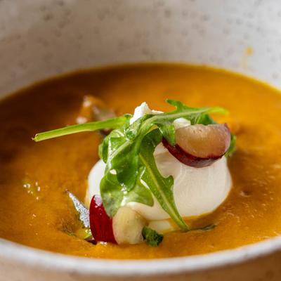 Roasted carrot soup topped with goat cheese, arugula, and grapes.