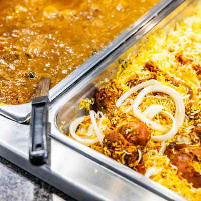 Buffet trays with flavorful curry on the left and vibrant biryani with onions on the right.