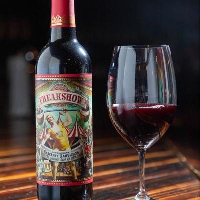 A bottle and glass of red wine on a wooden surface.