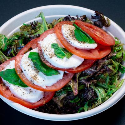 Caprese salad with greens, tomato slices, mozzarella, and basil.