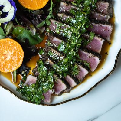 Sesame-Crusted Seared Tuna Tataki dish accompanied by mixed greens and citrus slices.
