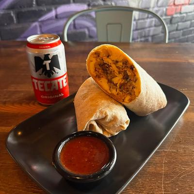 Chicken burrito cut in half served with red salsa and a can of beer.