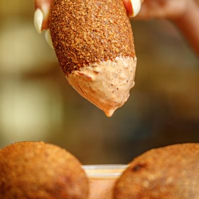 Close-up of a fried kibbeh ball dipped in a creamy sauce.