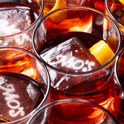 Amber colored drinks with ice cubes and citrus garnishes in glasses.