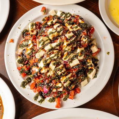 Chopped salad with cheese cubes, pesto, and balsamic drizzle on a white plate.