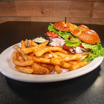 Turkey club croissant with bacon, lettuce, tomato, side of fries and a dip.
