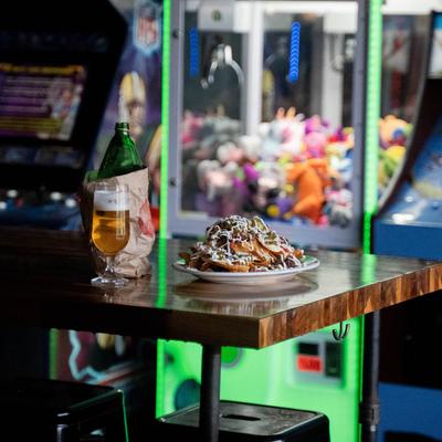 Loaded nachos served on a table and a beer, arcade machines in the background.