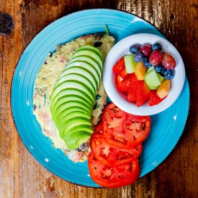 Mediterranean Omelet with fresh avocado on top, tomato and fruit cup, top view.