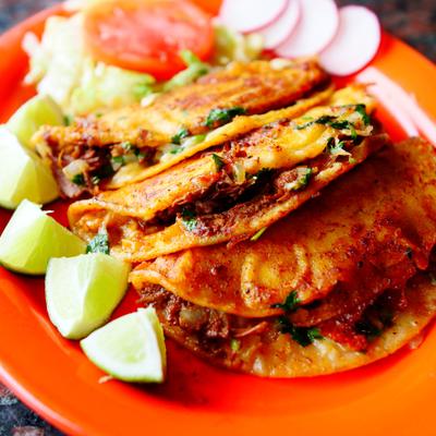 Taco Birria plate with lime wedges and fresh vegetables on the side.