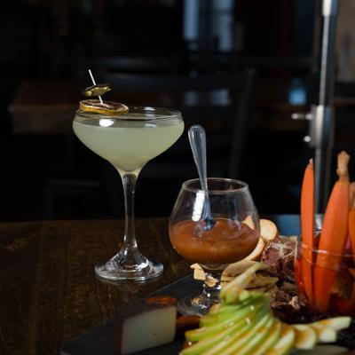 A pale green cocktail in a stemmed coupe glass, a small sauce goblet and a charcuterie board.