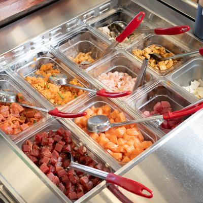Seafood ingredient station with diced fish and toppings in metal trays.