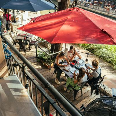 Guests seated at a table under a red umbrella on a wooden deck.