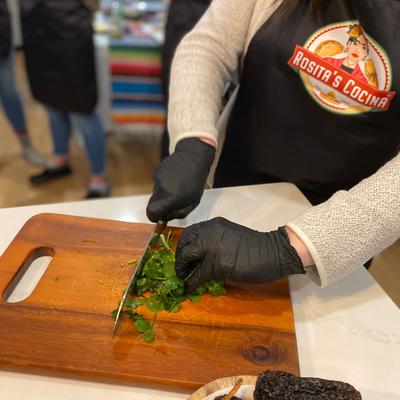 A cooking student wearing  a Rosita’s Cocina apron  cutting cilantro with a knife.