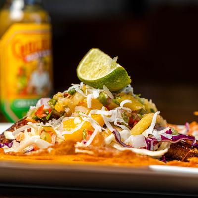 Pina Colada Tilapia Taco with hot sauces in the background.