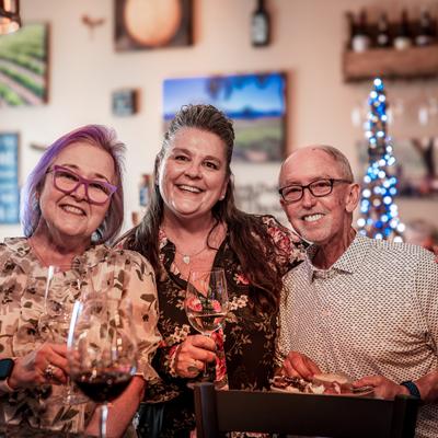 Three people smiling together with wine glasses.