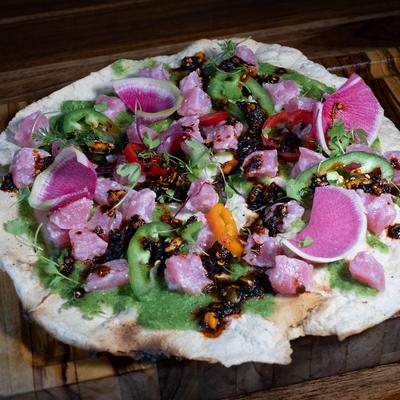 Flatbread topped with raw tuna, radish, green sauce, peppers, and salsa macha.