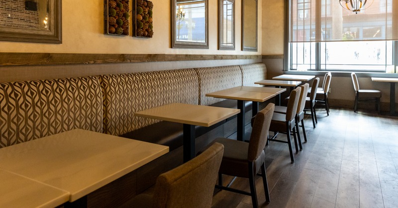 Interior, banquette seating by a decorated wall, lined up tables and seats