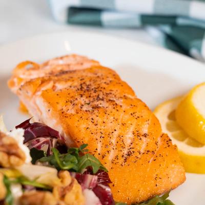 A close-up of a seared salmon with salad and lemon slices.