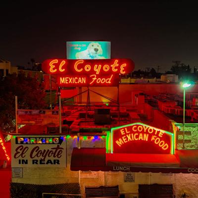 Red neon El Coyote Mexican Food signs on a building at night.