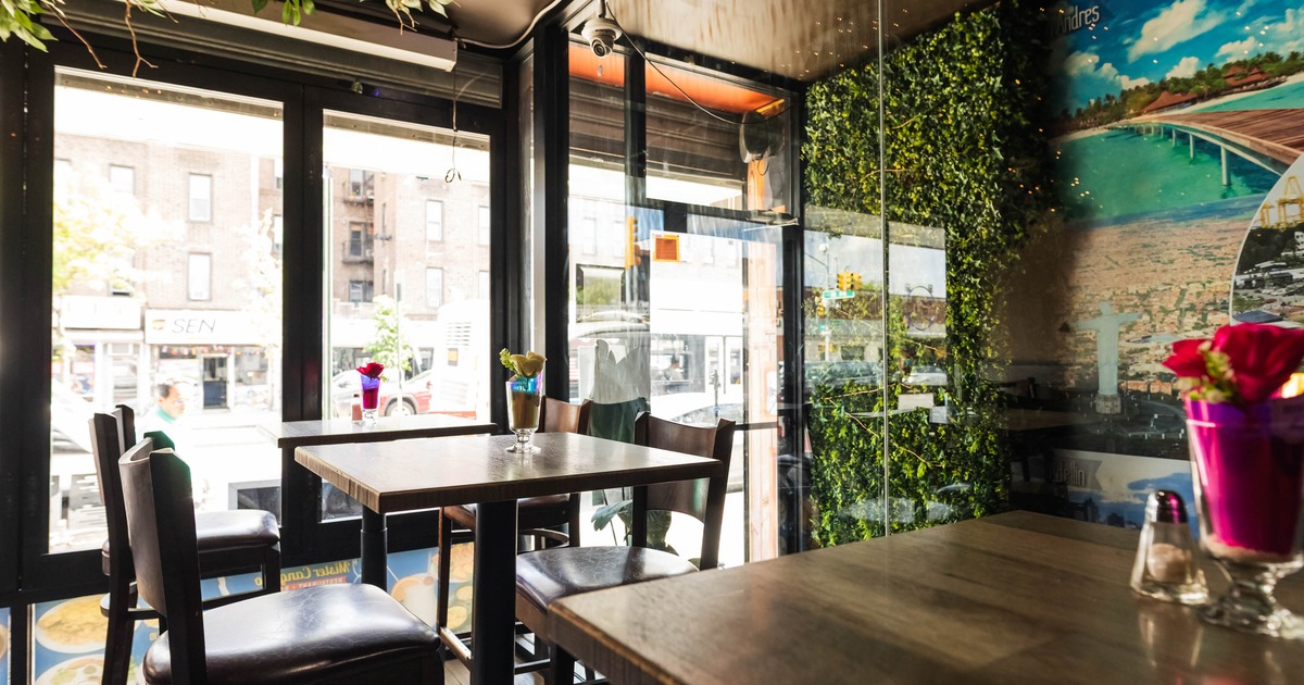 Interior of a café with wooden tables, chairs, large windows, green foliage on the ceiling