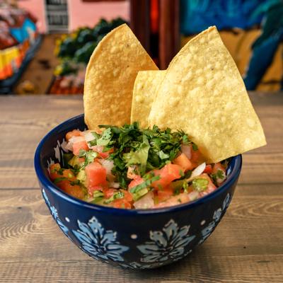 Bowl of Guacamole topped with pico de gallo and tortilla chips.