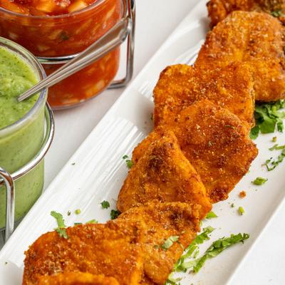 Fish Pakora on a long white plate next to three chutneys.