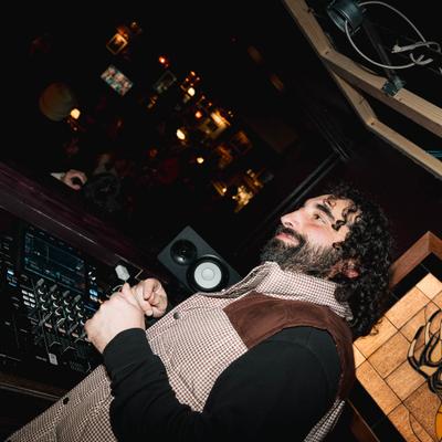 A DJ smiles while DJing in a dimly lit room.