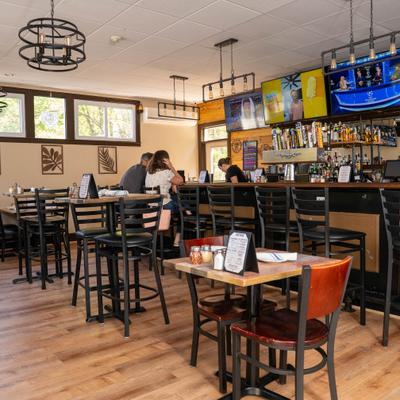Bright restaurant interior featuring bar seating, multiple TVs, and pendant lights.