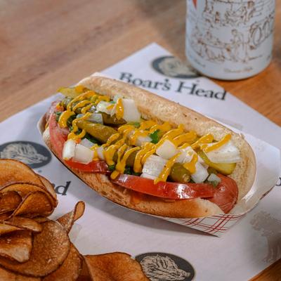 Hot dog topped with pickles, onions, and mustard served with potato chips.